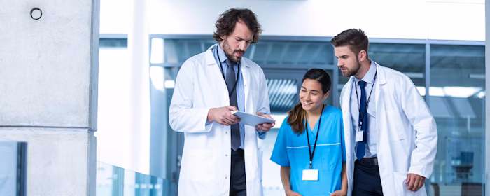 Three healthcare professionals reviewing information on a tablet in a medical facility