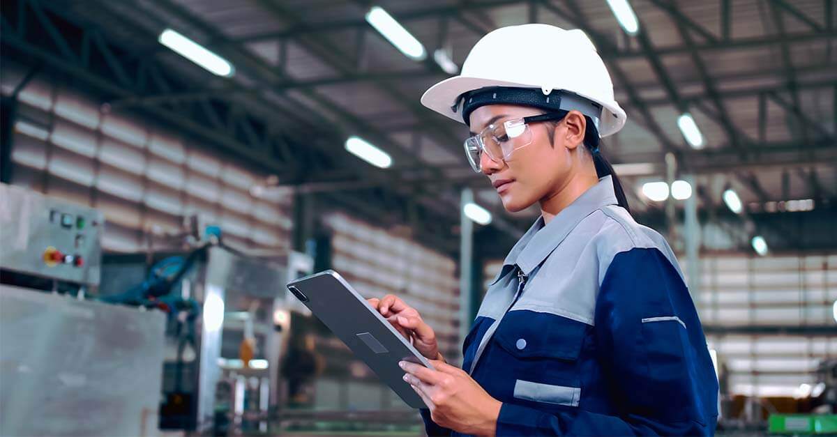 Female engineer in a hard hat using a tablet inside an industrial facility.
