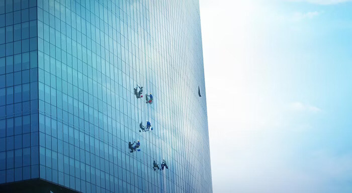 Workers suspended on ropes cleaning the glass facade of a tall skyscraper under a clear sky