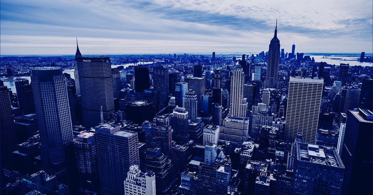 A high-angle view of a densely packed city skyline, with skyscrapers and tall buildings under a cloudy sky, showcasing an urban metropolis.