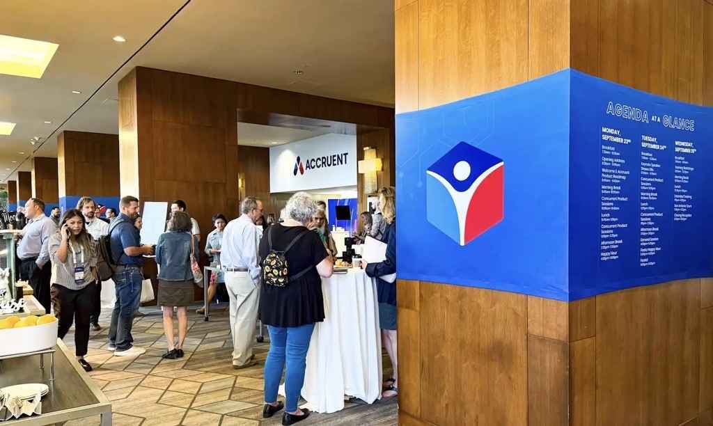 Attendees networking at an Accruent conference with an agenda display in the background.