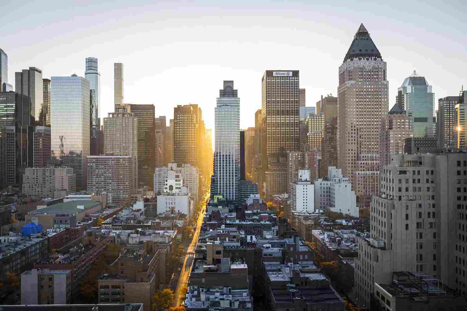 A city skyline at sunset with high-rise buildings and a sunlit street