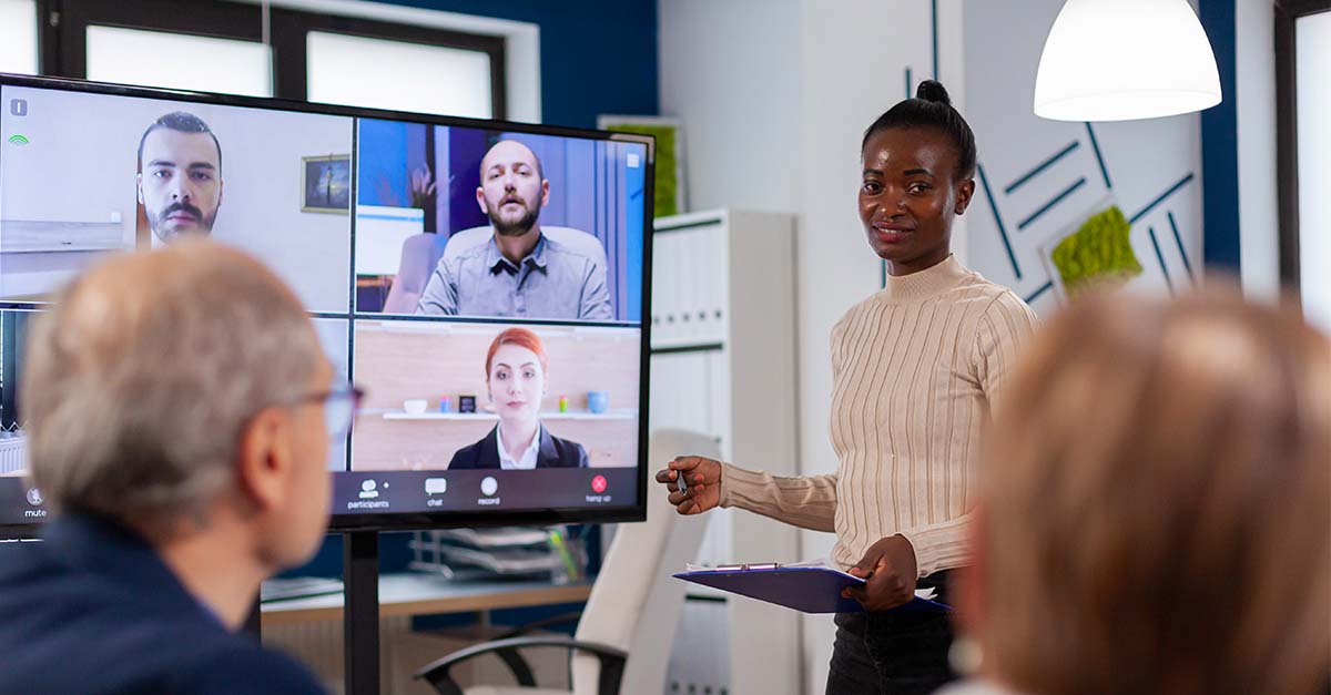 woman presenting to team in conference room and with listeners over video conferencing