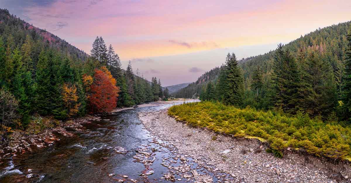 Scenic river flowing through a forested valley at sunset with autumn foliage.