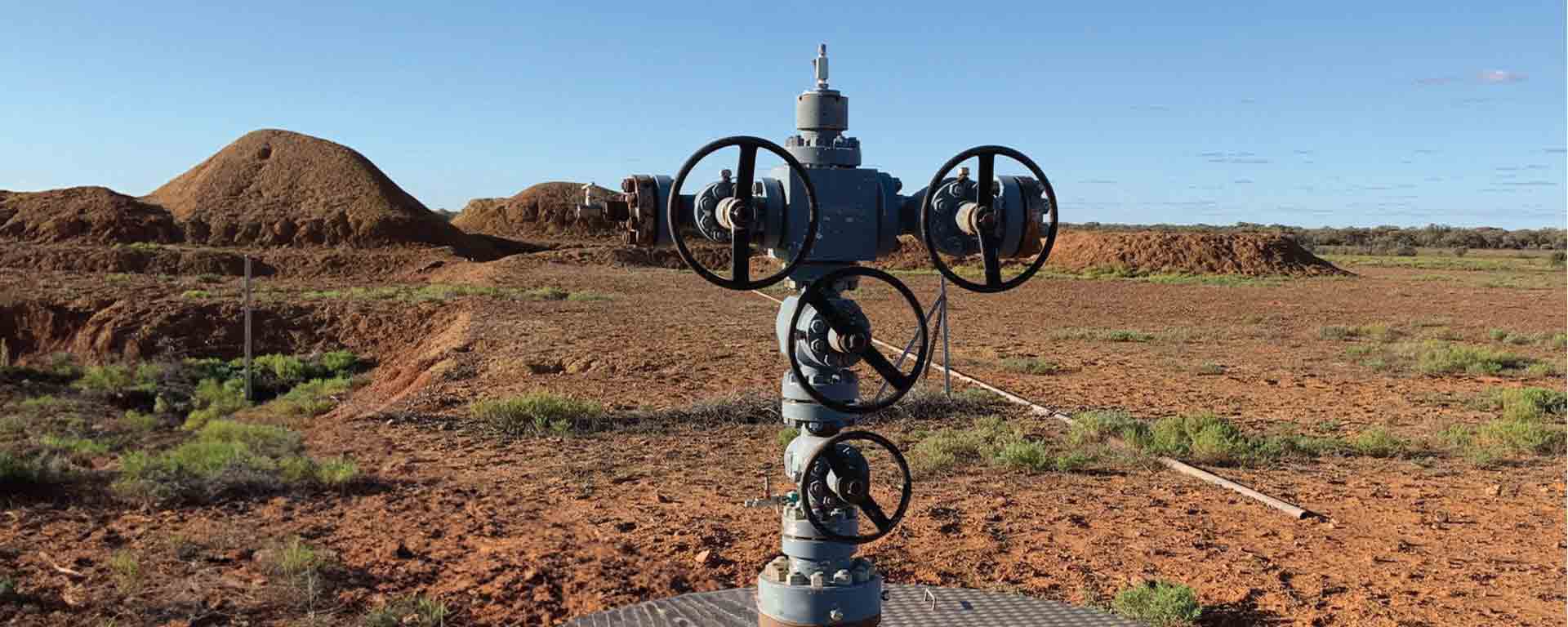 An isolated wellhead with multiple valve controls standing in a dry, open landscape, used for oil or gas extraction in a remote industrial site.