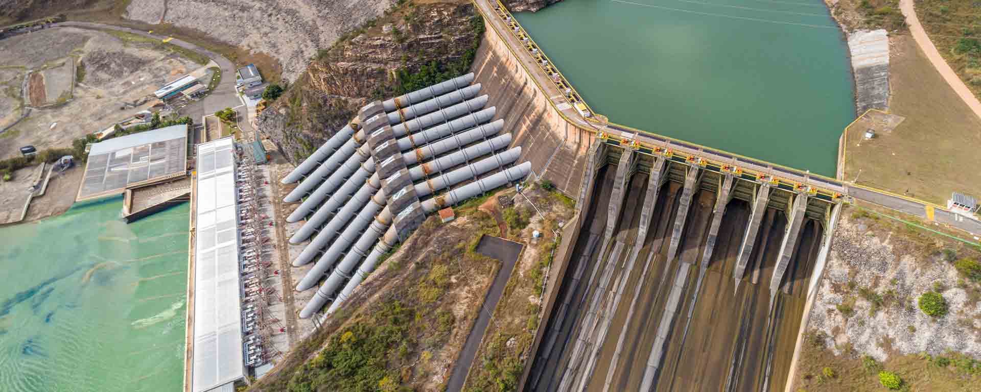 Aerial view of a hydroelectric dam with large penstock pipes and a reservoir.