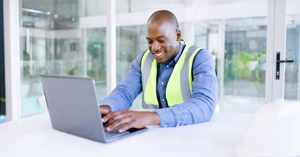 Smiling construction worker in a safety vest using a laptop in a modern office