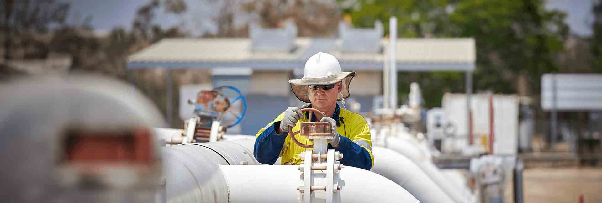 Worker in safety gear adjusting a pipeline valve at an industrial site.